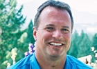 A man with a blue shirt smiles at the camera.