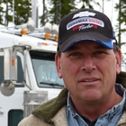A guy will a black ball cap standing in front of a white semi truck.