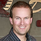 A man stands beside a desk and company sign.