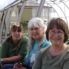 three women pose in front of a greenhouse
