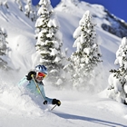Woman skies through deep powder against snowy trees and a blue sky.
