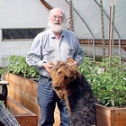 The Haagerup family sits in their greenhouse around plant boxes and smile. Bent is holding the paws of a big dog.