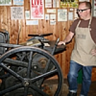 Man standing beside an old-fashioned letterpress machine in Fernie, BC
