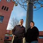 a man and woman near a tree sculpture and clock tower