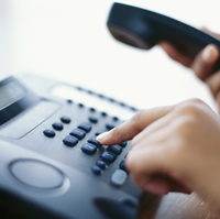 A black phone is held off the hook while a number is dialed.