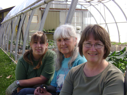 three women pose in front of a greenhouse