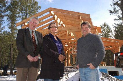 Two men and one woman in front of timber-frame structure