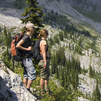 Two girls in hiking gear stand looking over an epic mountain landscape.