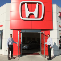 Two men stand at either side of a red entry emblazoned with the Honda symbol.