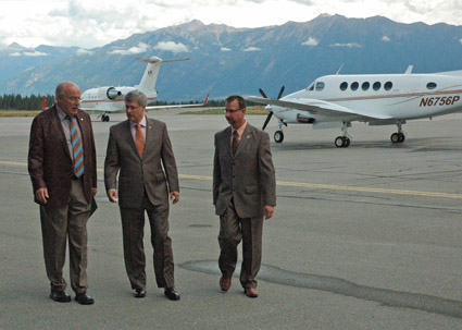 Three men in suits walk across the tarmac with two planes and mountains in the background.